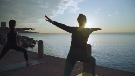two women doing sunrise yoga at the lake. slow motion.