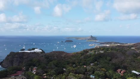 lateral movement with drone on the island of fernando de noronha, lighthouse and boats in the background, blue sky and sunny day, view of the fort