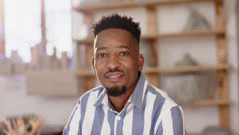 Happy-african-american-man-with-beard-sitting-and-smiling-in-pottery-studio,-slow-motion