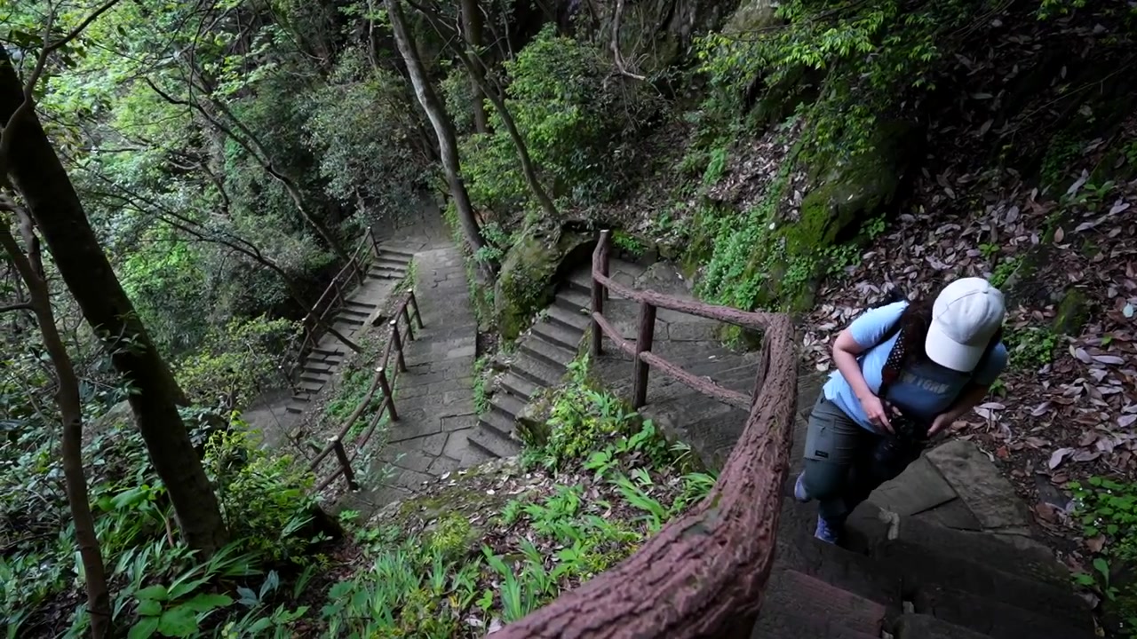 Young woman climbing stone stairs on a hiking trail in a lush forest at Huangshi Village