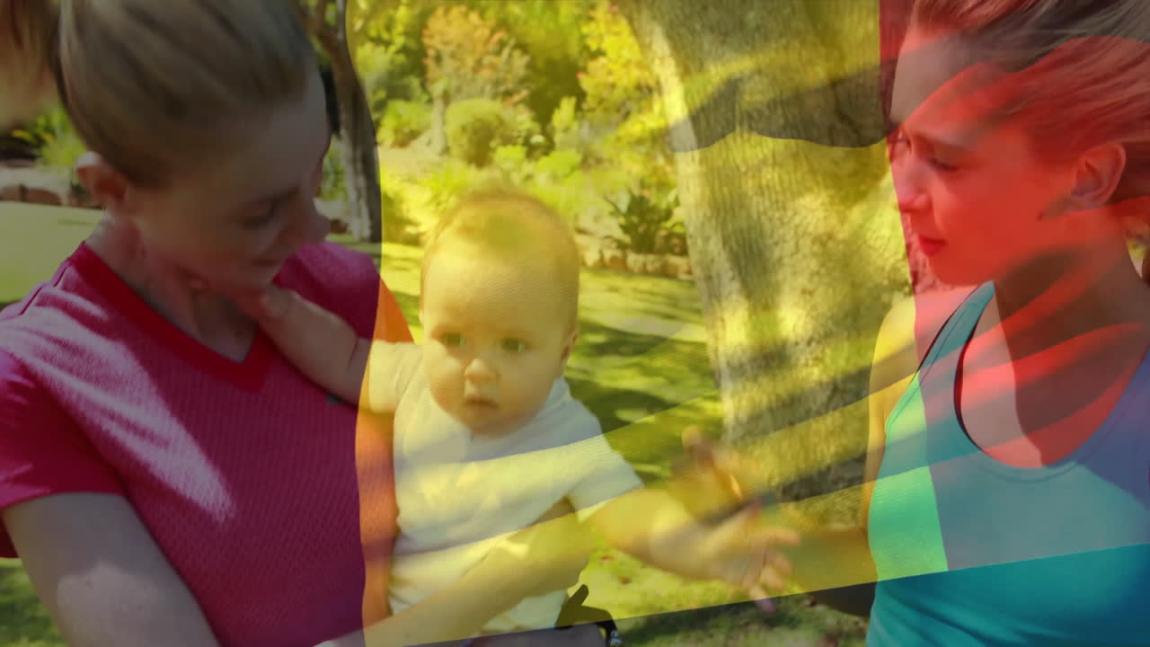 Two women holding baby in park with colorful abstract overlay animation