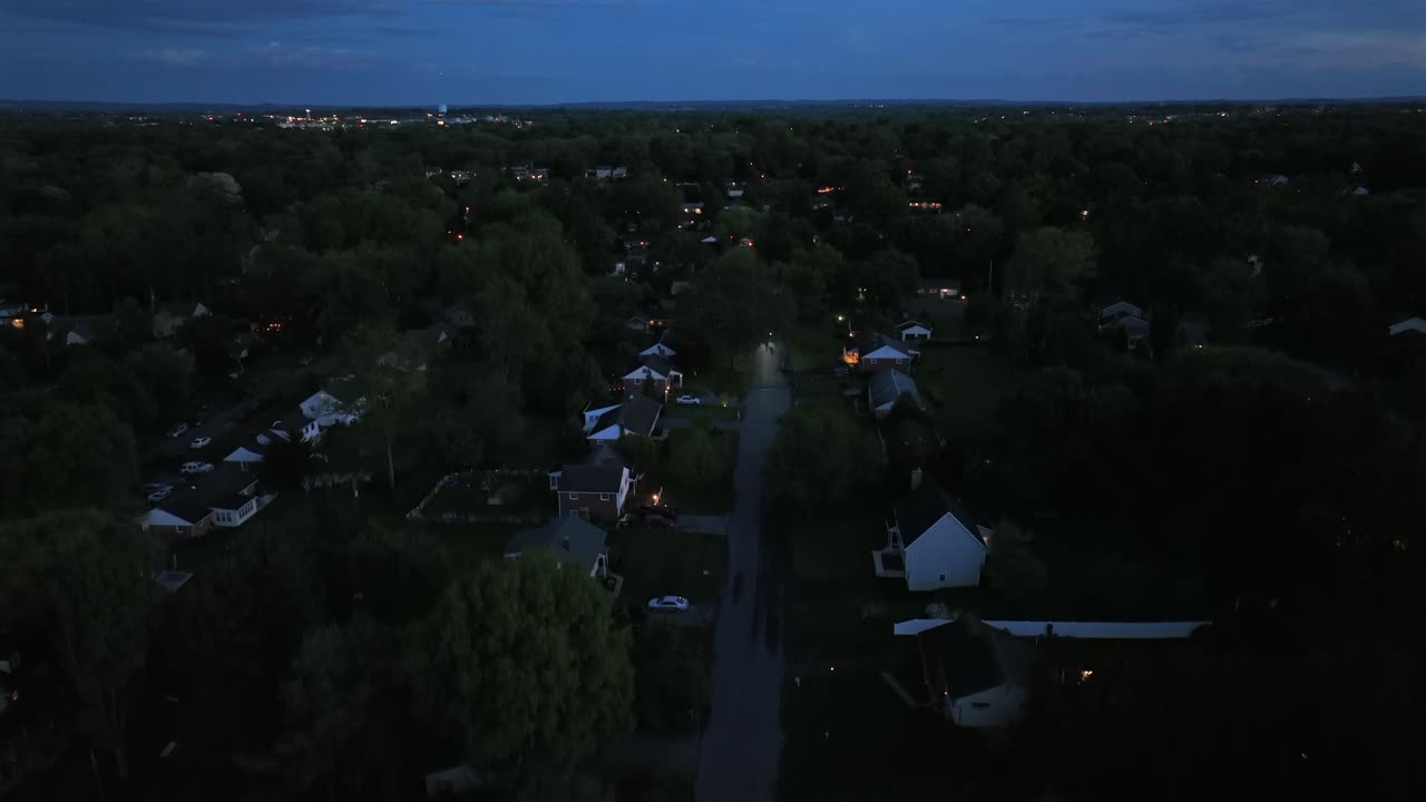 Single family houses at night. Twilight aerial view of a quiet suburban street with two-story houses. Green trees on spring day in May. Aerial rising wide shot. Quiet neighborhood scene.