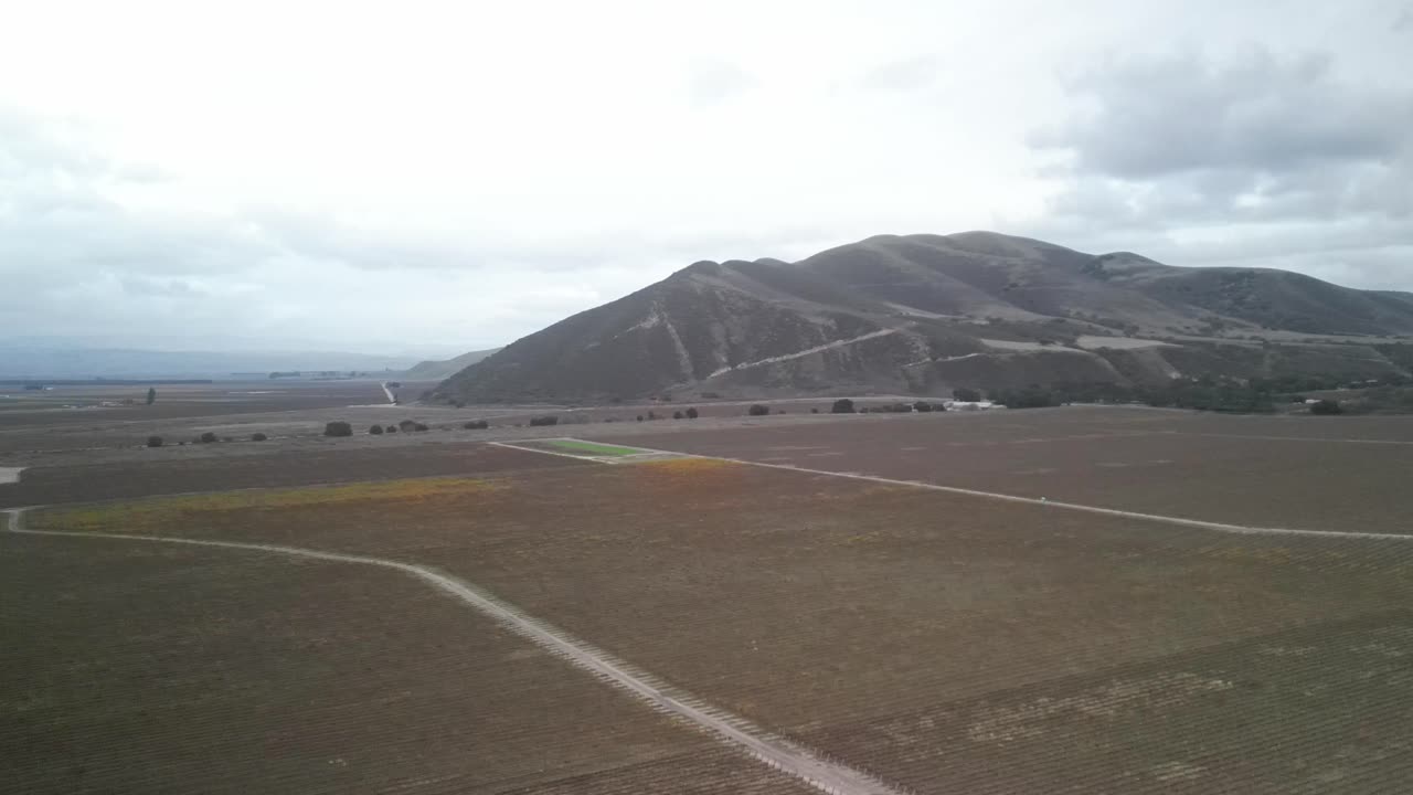 la llanura de sicómoro en greenfield, california, mostrando campos agrícolas, sobre un cielo nublado, capturando la esencia del paisaje del valle de salinas con montañas en el fondo, toma de panorámica aérea