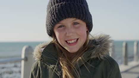 portrait of happy little girl on beach laughing cheerful dressed warm wearing beanie hat and coat