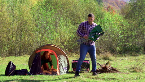 boyfriend sitting on camping seat while girlfriend preparing the tent