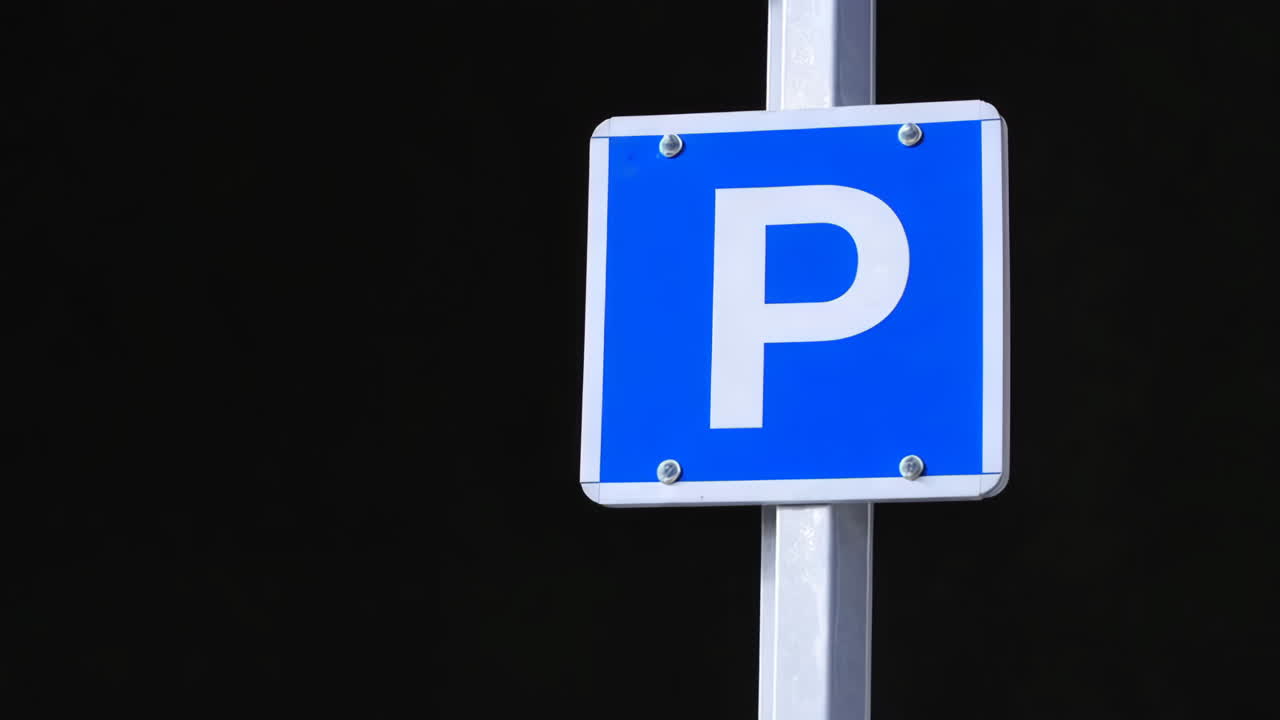 En blå parkeringsskylt med ett vitt 'P' mot en mörk bakgrund