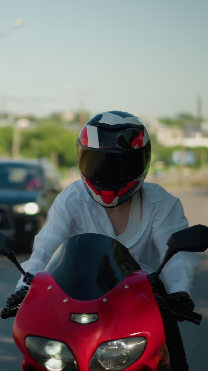 una motociclista femenina en una bicicleta eléctrica roja viaja a través de un área urbana, su camisa abierta por el viento, revelando su singlet y cuerpo, se ve un coche siguiendo por detrás