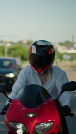 una motociclista femenina en una bicicleta eléctrica roja viaja a través de un área urbana, su camisa abierta por el viento, revelando su singlet y cuerpo, se ve un coche siguiendo por detrás