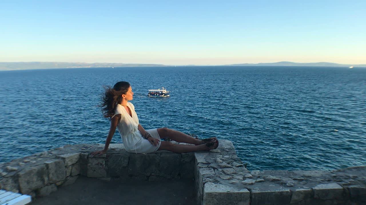 Pretty young woman sitting in the rocks and enjoying the stunning view of Adriatic sea, Split, Dalmatia, Croatia