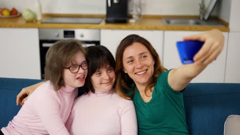 woman taking a selfie with her daughters with down syndrome sitting on the sofa in the living room