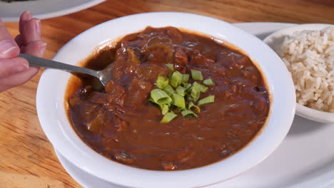 woman takes a spoonful of gumbo, spoon scoops a biteful of dark rich cajun gumbo, slider hd