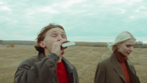 couple walking on field and drinking from hip flask