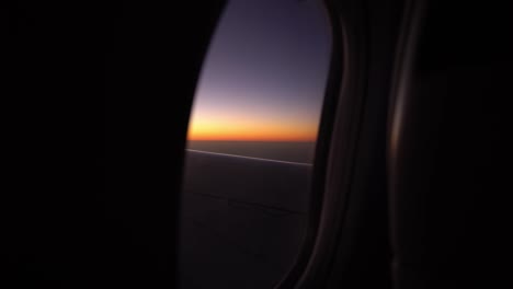 view from porthole plane flies over sky at sunset or sunrise, the view from the window on the wing of the airplane and flaps.