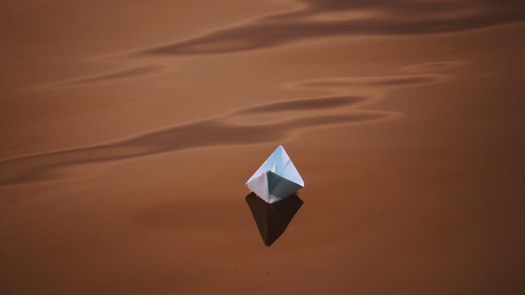 Dark background of water surface and paper ship floating in the evening. Homemade paper boat swimming outdoors at sunset.