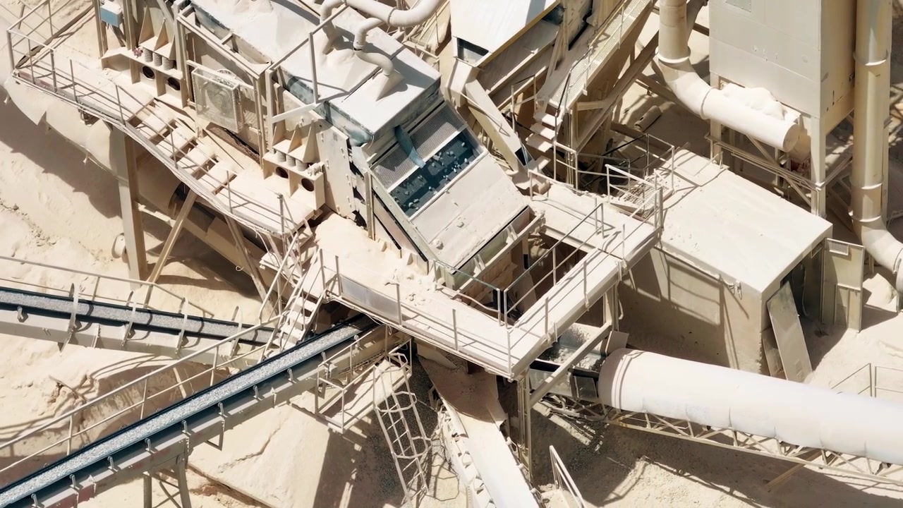 Heavy machinery transports limestone and aggregates through conveyor belts. Mining equipment operates in an open pit quarry. Industrial landscape showcases raw material processing.