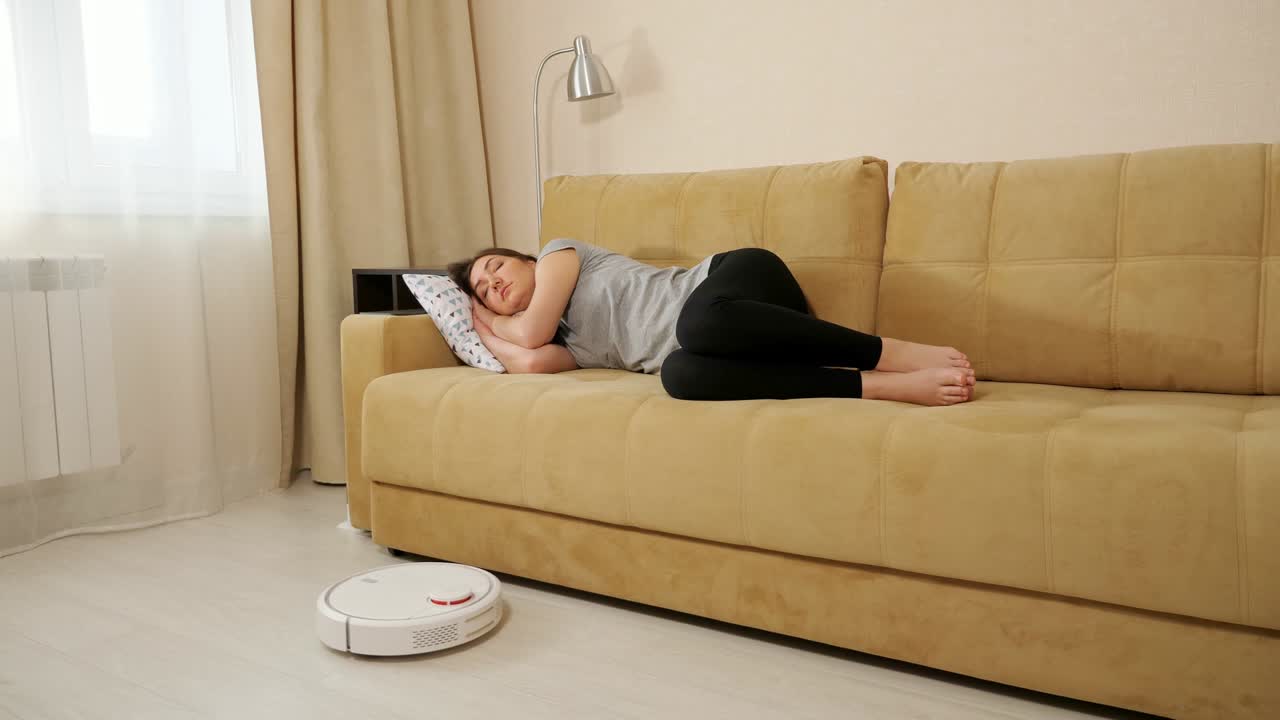 Brunette woman sleeping on the couch robot vacuum cleaner cleans the floor