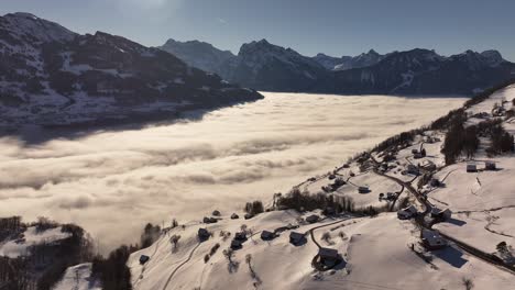 aerial view of amden, switzerland. the picturesque village nestled on the slopes of the walensee is shrouded in a dramatic sea of fog, with snow-capped mountains rising majestically in the distance.