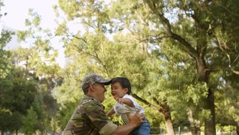 military dad in camouflage clothes playing airplane with son and the mother is watching them