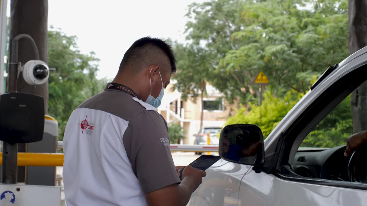 guardia de seguridad privado mexicano latinoamericano verificando la identificación de una persona con una tableta y una cámara de seguridad mientras conduce su furgoneta a un complejo privado