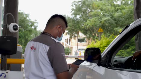 Guardia-De-Seguridad-Privado-Mexicano-Latinoamericano-Verificando-La-Identificación-De-Una-Persona-Con-Una-Tableta-Y-Una-Cámara-De-Seguridad-Mientras-Conduce-Su-Furgoneta-A-Un-Complejo-Privado