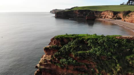 Impresionante-Bahía-De-Ladram:-La-Cámara-Se-Desliza-Lentamente-Hacia-Atrás-Sobre-Escarpados-Acantilados,-Revelando-Fascinantes-Vistas-De-Las-Costas-Rocosas-Y-La-Tranquila-Bahía