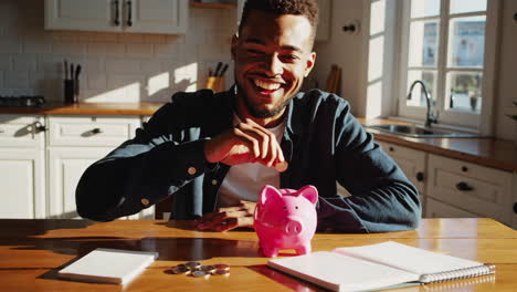 a happy man saving money in a pink piggy bank at home