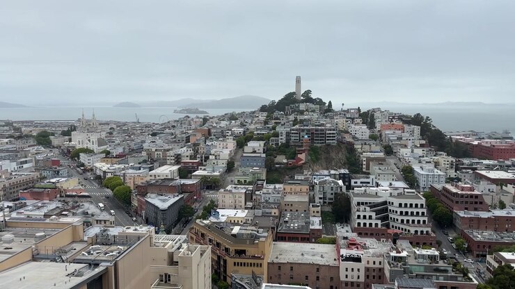 Ripresa statica dell'iconico skyline di North Beach con la Coit Tower, edifici cittadini raggruppati e le acque della baia in lontananza sotto un cielo cupo e nuvoloso per uno storytelling urbano