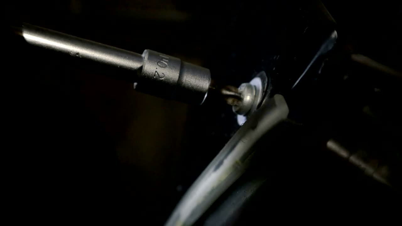 - un primer plano de una vista en primera persona de un destornillador de metal envolviendo el perno en una motocicleta de plástico negro en su propio garaje, servicio