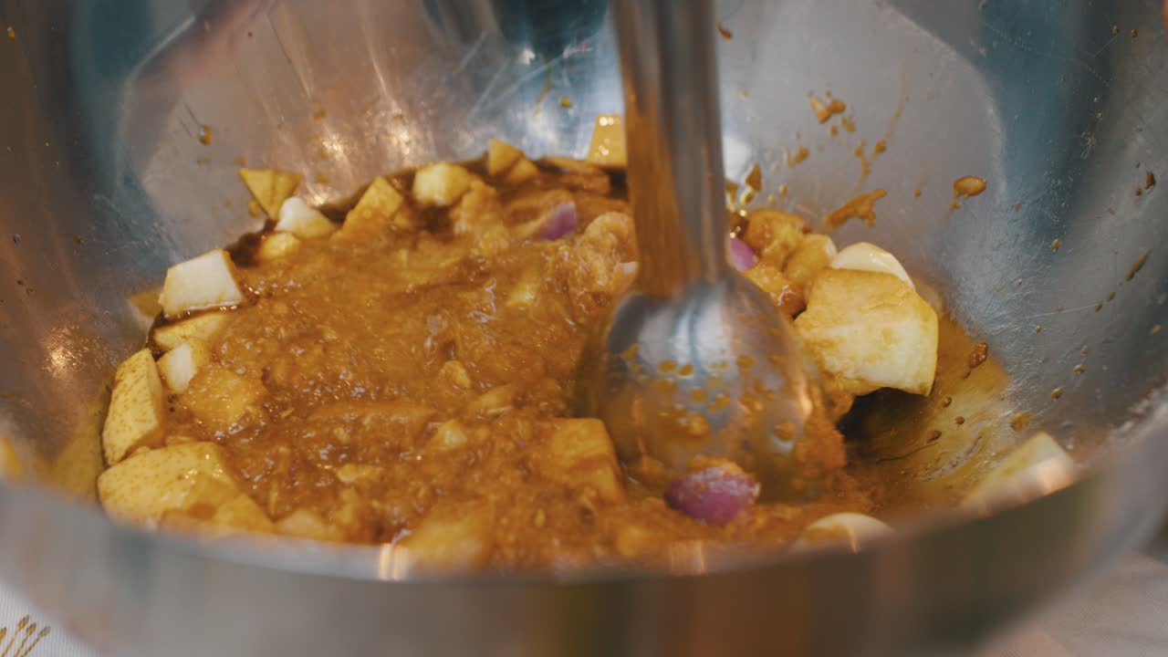 machacar ingredientes de pera, cebolla y ajo con batidora eléctrica dentro de un recipiente de metal profundo