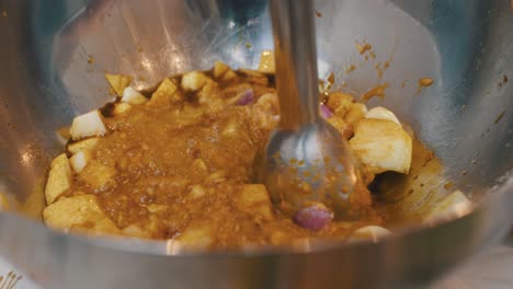 Mashing-pear,-onion-and-garlic-ingredients-with-electric-blender-inside-deep-metal-cooking-bowl