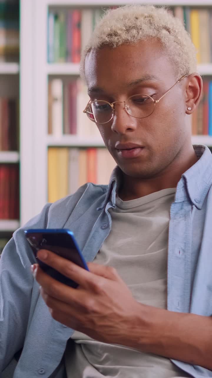 Young man engaged with smartphone in a cozy library setting