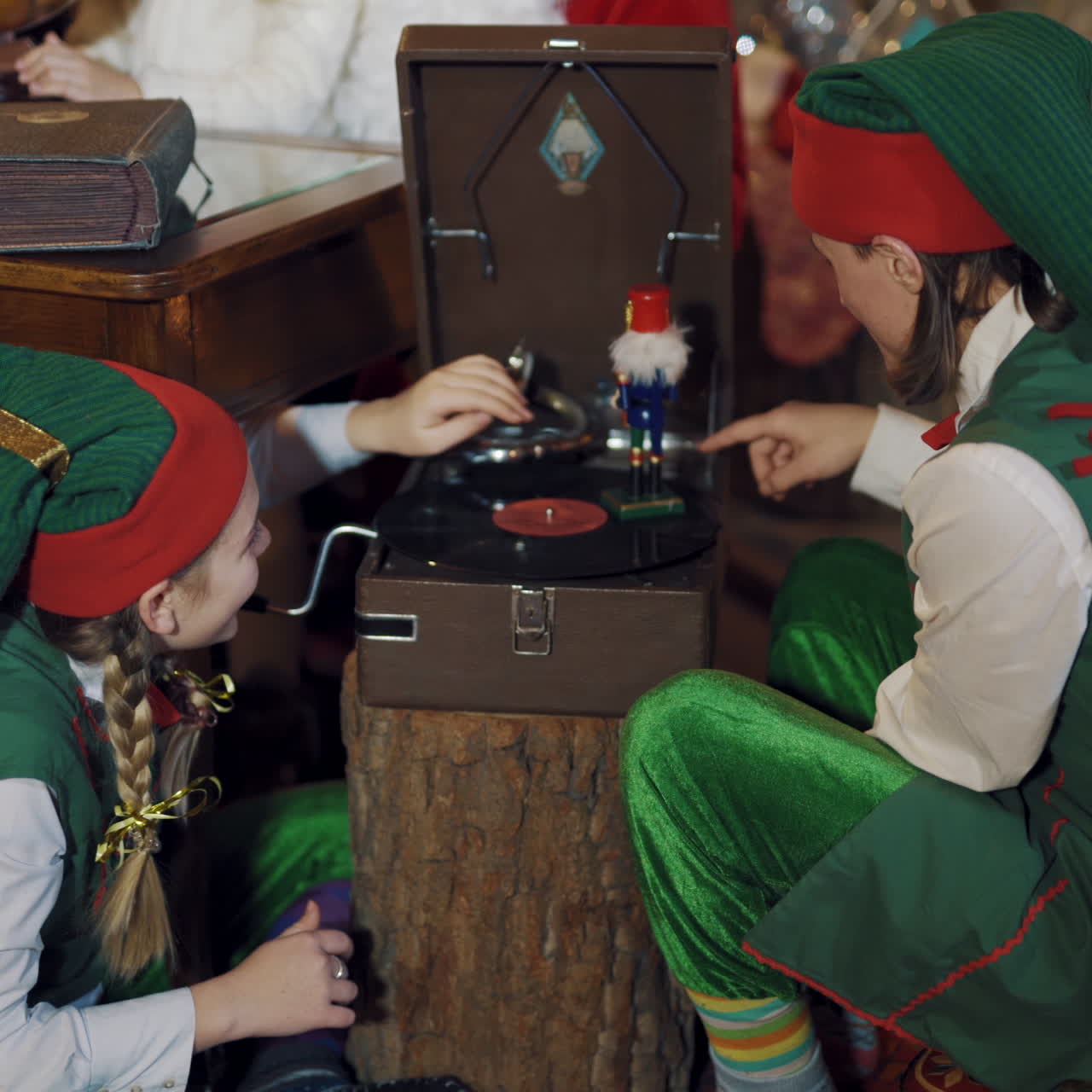 Funny elves in fairy costumes play with a toy indoors. Two elves male and female spinning a disk on the old recorder with toy soldier in Santa's residence.