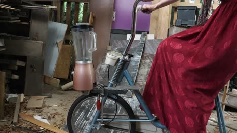 Smiling-Beautiful-woman-Eco-Conscious-Hippie-pedalingope-On-upcycled-repurposed-Bike-running-a-human-powered-blender-Inside-Shed