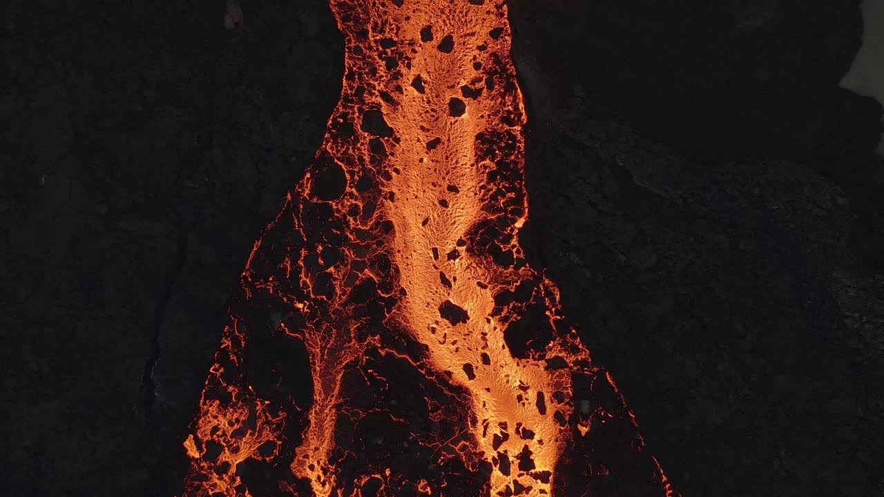 Fiume di lava che scorre lungo un paesaggio vulcanico nero