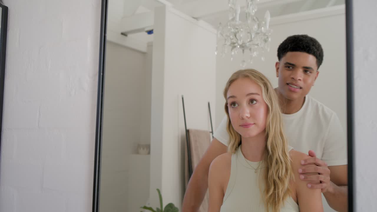 Coppia allo specchio del bagno, uomo afroamericano che indica, donna che si tampona il viso controllando la pelle