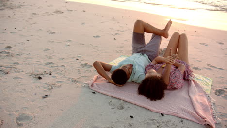 pareja biracial se relaja en una toalla de playa al atardecer con espacio de copia