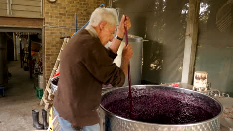 man stirs grapes fermenting in a barrel before producing red wine