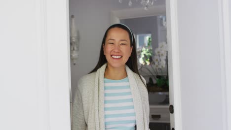 Happy-asian-woman-opening-front-door,-smiling-and-greeting-visitor-to-home