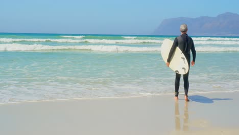 Rear-view-of-active-senior-Caucasian-male-surfer-walking-with-surfboard-on-the-beach-4k