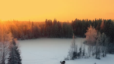 Golden-sky-sunset-over-remote-European-forest,-snow-covered-landscape,-drone