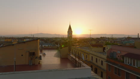 Slide-and-pan-footage-of-tower-protruding-above-other-buildings-in-city.-Aerial-morning-shot-against-rising-sun.-Rome,-Italy