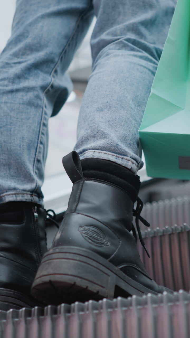움직이는 에스컬레이터에서 청바지와 인 부츠의 클로즈업, 앞에 있는 사람들의 흐릿한 그림, 일상적인 도시 생활의 순간을 포착합니다.