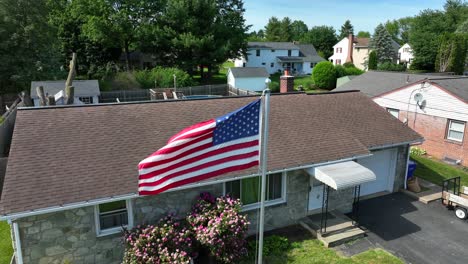 a drone rises over an american flag in front of a suburban home in a small town in america