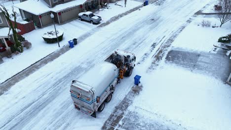 Toma-Aérea-De-Un-Camión-Recogiendo-Basura-En-Un-Barrio-Suburbano-Cubierto-De-Nieve