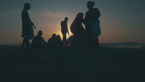 young tourists set up camp near burning bonfire at sunset