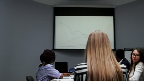un joven empleado de la empresa con una camisa blanca informa sobre el progreso del trabajo realizado en el último año y los planes de desarrollo para el trimestre ocupado en el diagrama del proyector en la oficina. informe a la junta directiva un equipo multiétnico