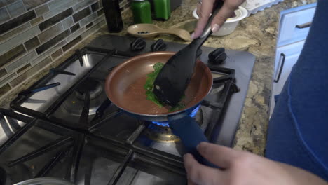 a woman cooking spinach in a non stick pan over a gas stove