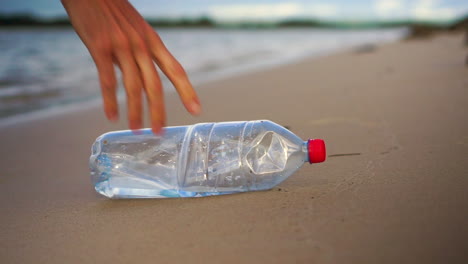 Nahaufnahme-Einer-Plastikflasche-Am-Ruhigen-Sandstrand,-Die-Von-Einer-Person-Abgeholt-Wird