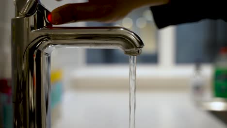 hand on hot water button on mixer tap with water being poured