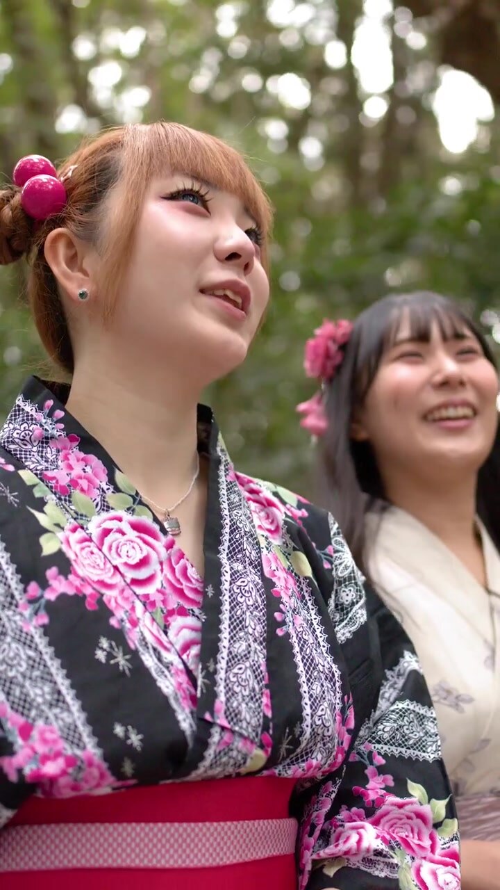 Due donne giapponesi che indossano kimono floreali sorridono e guardano verso l'alto in una lussureggiante foresta verde.
